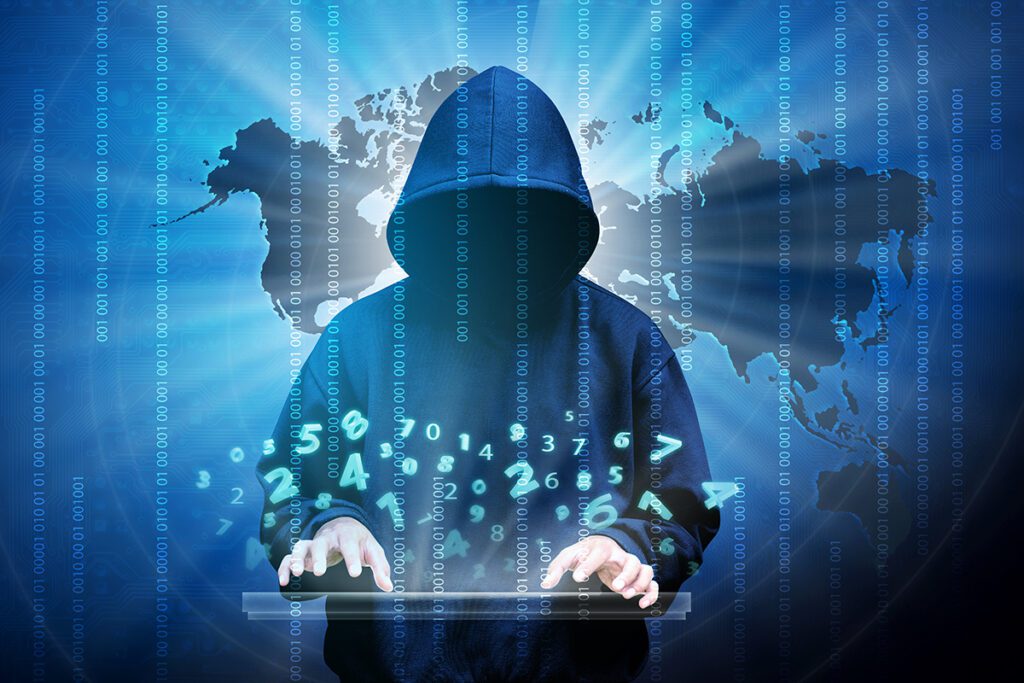 The silhouette of a computer hacker against a world map.
